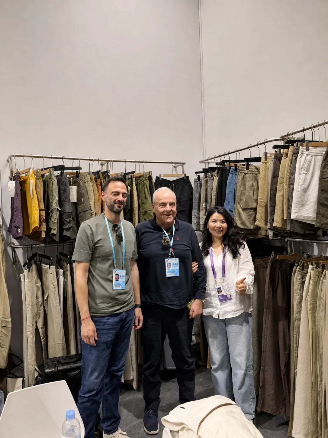 Three people posing together in front of trouser displays at an exhibition booth