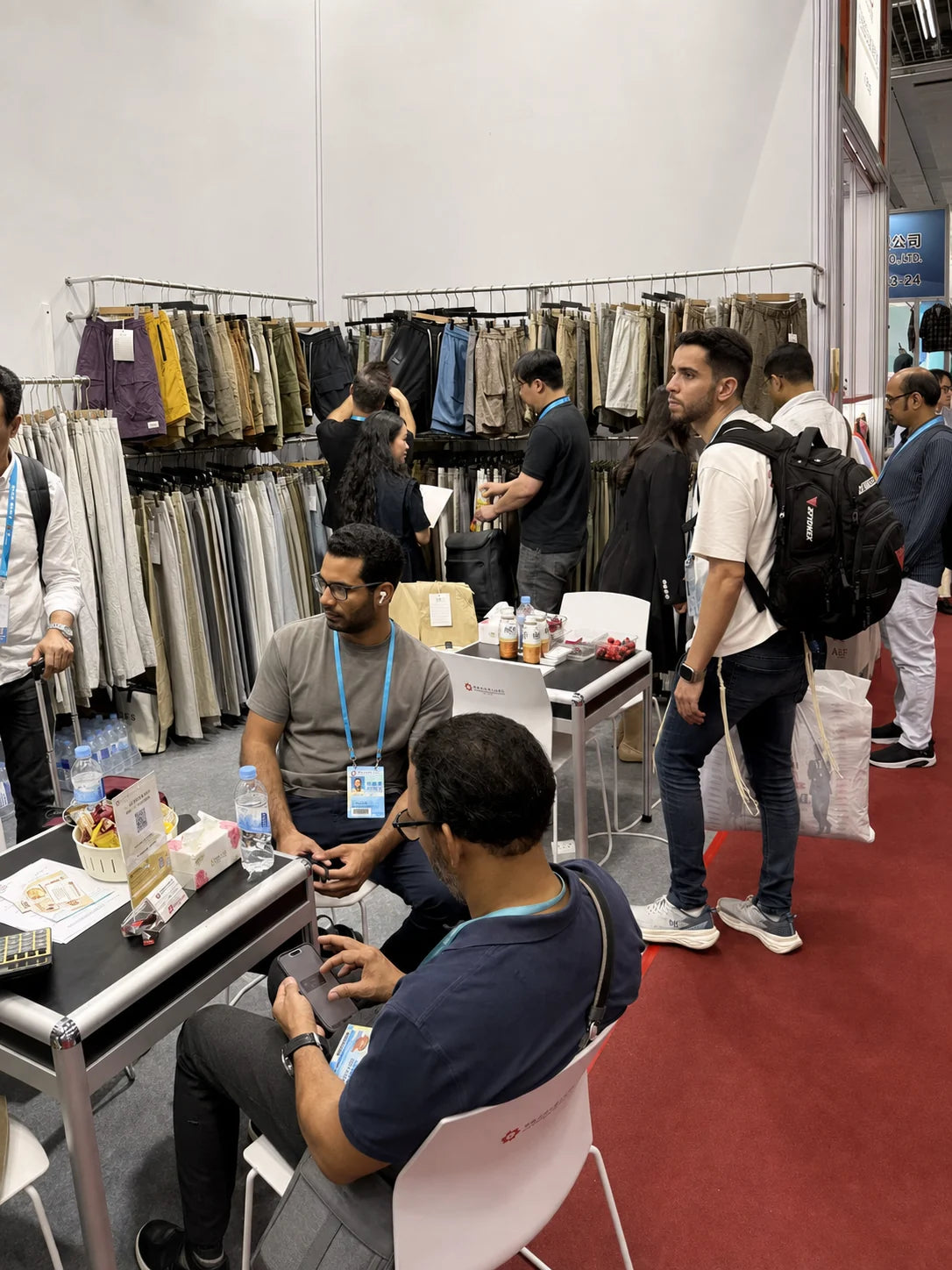 People beside racks of trousers and shorts at an exhibition booth