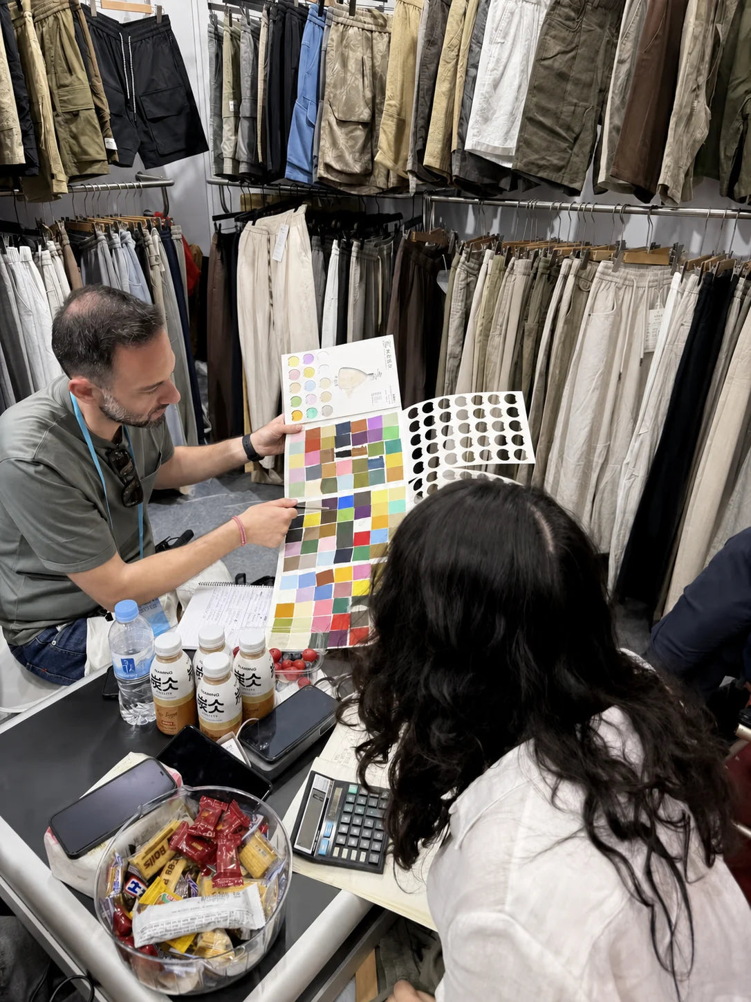 People discussing a spread of color cards beside racks of trousers